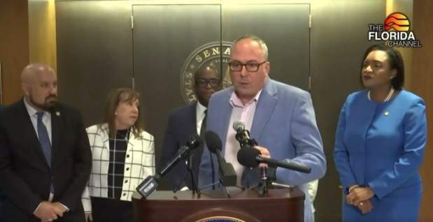 Michael Rajner discusses the AIDS Drug Assistance Program at a news conference outside the Florida Senate chamber on Feb. 25, 2026. Listening from left: state Rep. Mitch Rosenwald, Senate Democratic Leader Lori Berman, state Sen. Shevrin Jones, and House Democratic Leader Fentrice Driskell. (Florida Channel/courtesy)