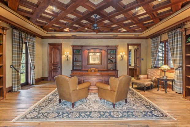 The formal office is separate from the main house and connected by a covered walkway. It has a wood coffered ceiling and multiple built-in bookshelves. (Photo by Michael Pelzer / Uneek Luxury)