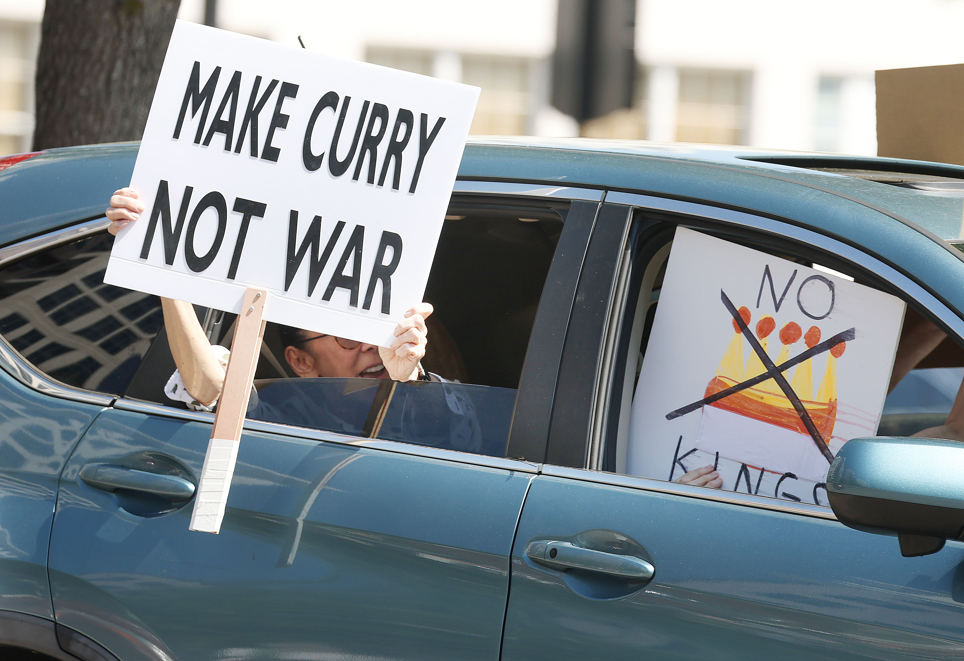 Protestors hold signs from inside a car as they join...