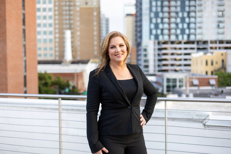 ortrait of Taryn Sabia standing on a rooftop balcony with the Tampa city skyline in the background. She is wearing a professional black blazer and smiling, with modern high-rise buildings and clear daylight behind her.