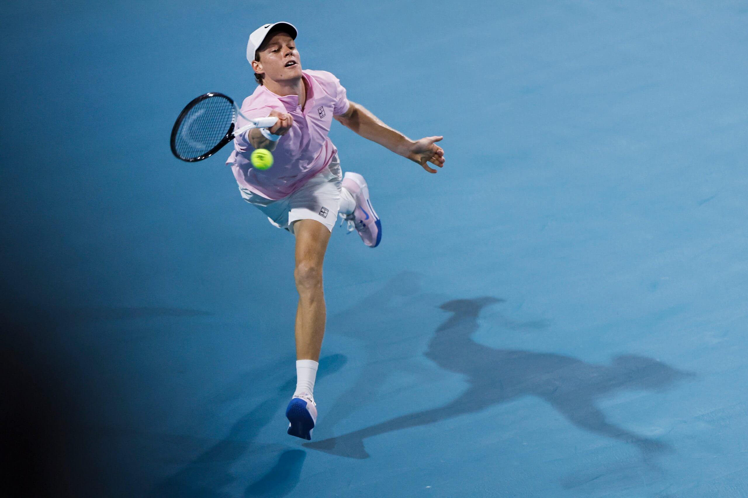 Jannik Sinner hits a forehand on the run on a blue hard court with his shadow to his left