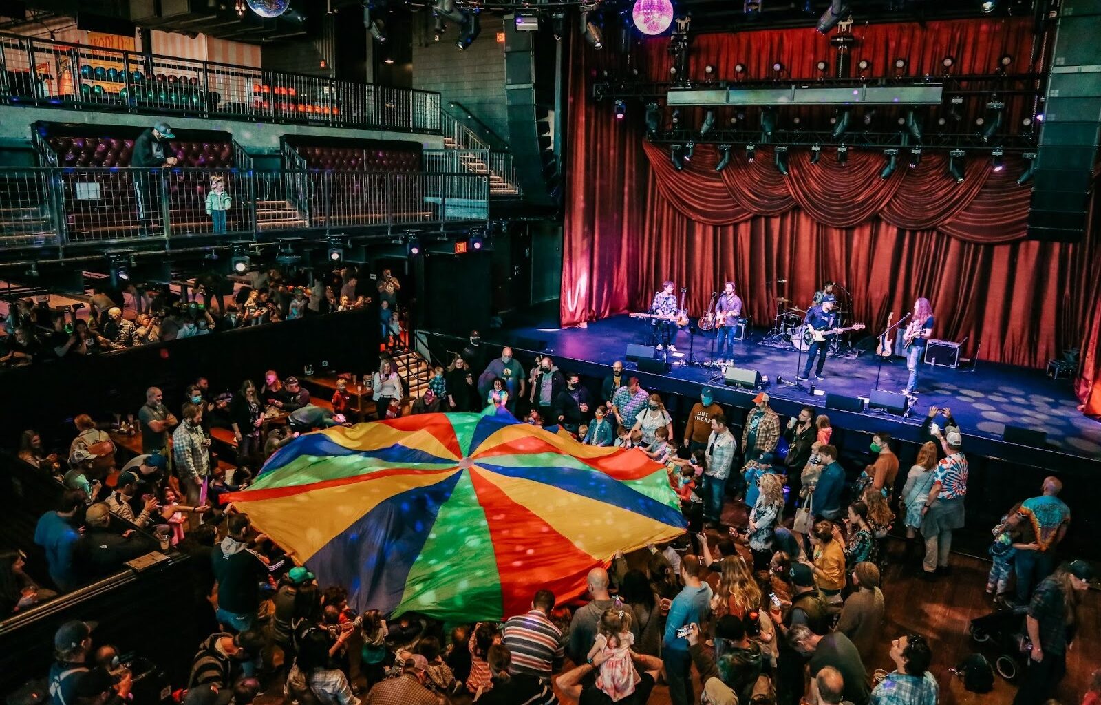 Photo of a concert with people holding a colorful fabric in the middle of the venue