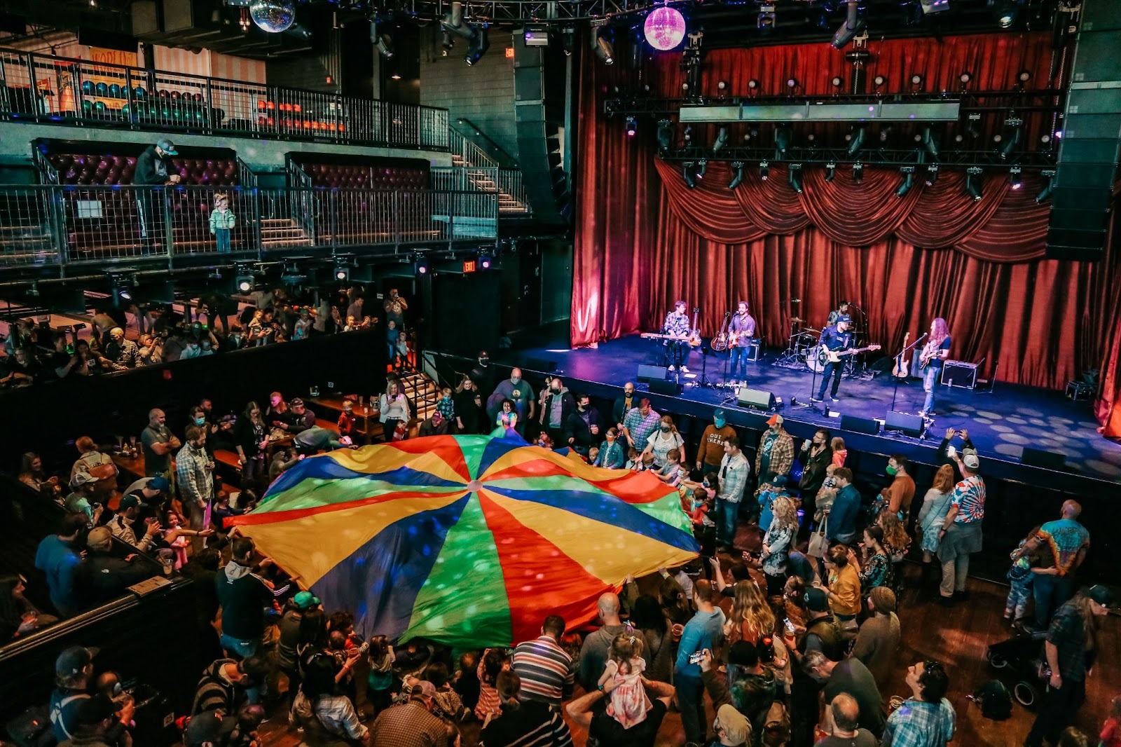 Photo of a concert with people holding a colorful fabric in the middle of the venue