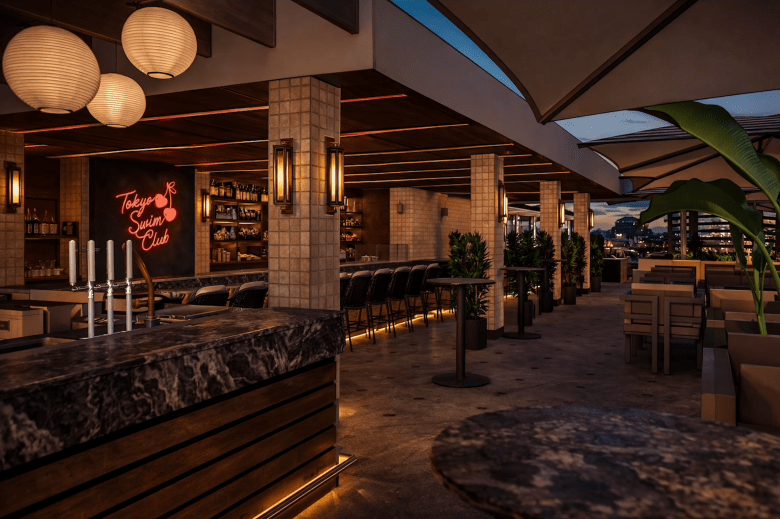 An interior-to-exterior rendering of Tokyo Swim Club rooftop lounge. The shot looks past the dark marble bar and modern lanterns inside toward the outdoor seating area, which is partially covered by sail shade structures under a deep blue twilight sky.