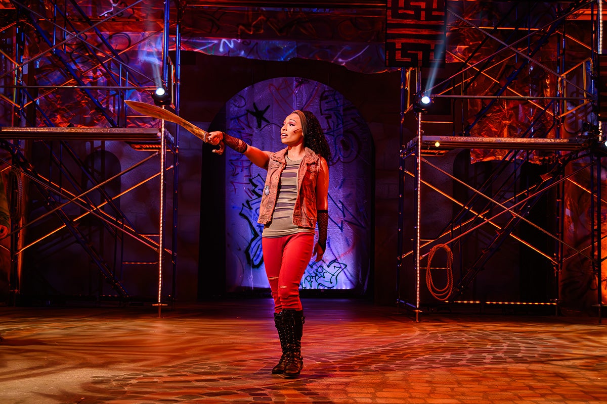 Black woman on stage confidently points sword 