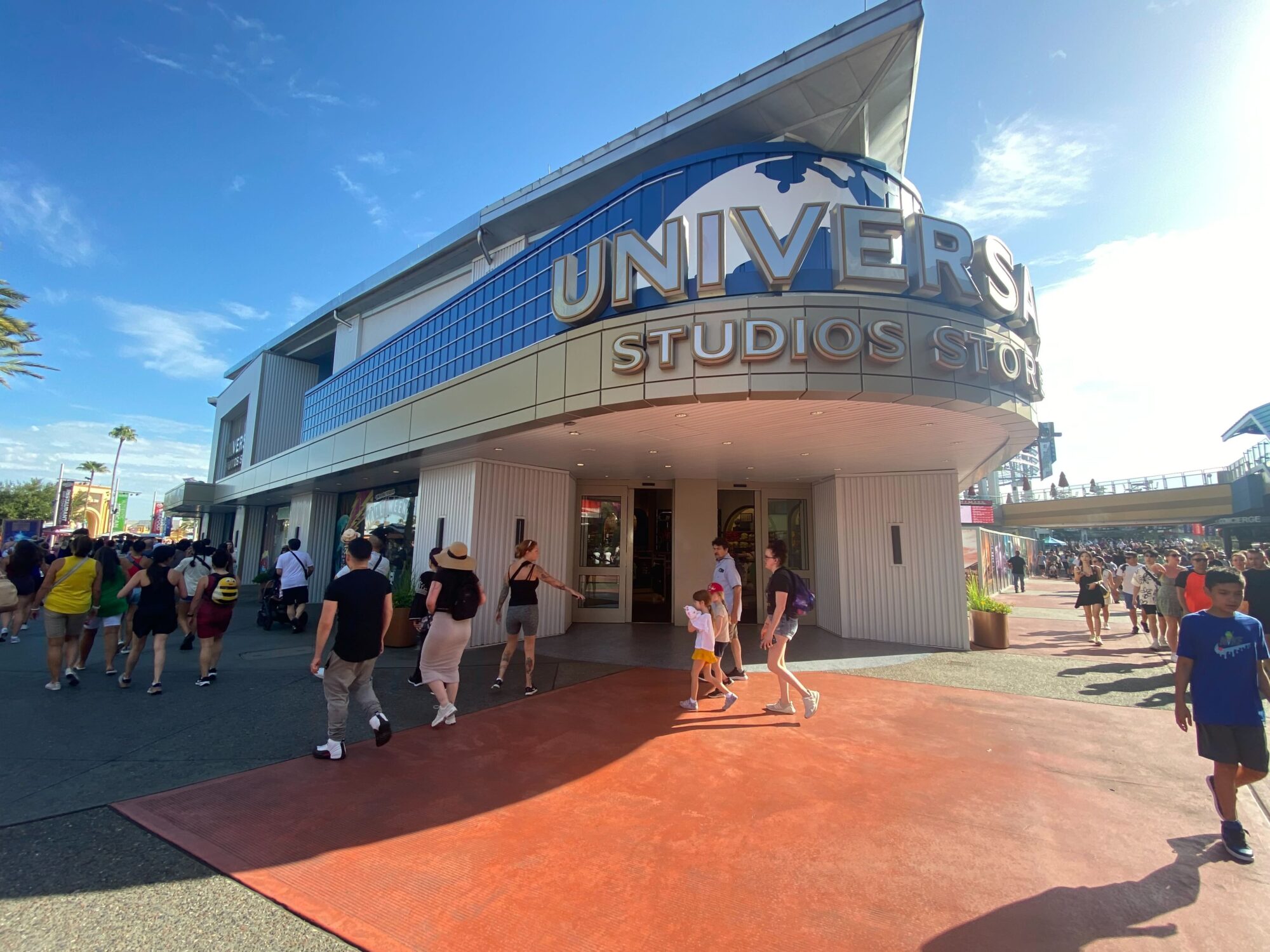 A crowd of people walk past the entrance to a Universal Studios store on a sunny day, eager to check out the latest Halloween Horror Nights merchandise inside.
