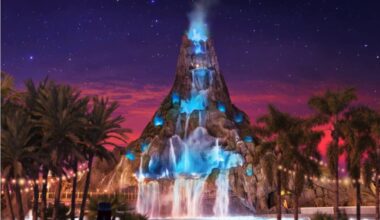A glowing volcano waterfall at night, lit with blue lights, surrounded by palm trees under a starry sky.