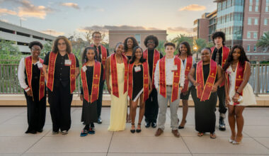 Group of students with garnet and gold sashes posing outside on the Student Union patio.