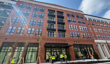 The Stevedore apartment building at Gasworx in Ybor City, a mid-rise brick residential development with ground-floor retail and workers gathered outside during a site tour.