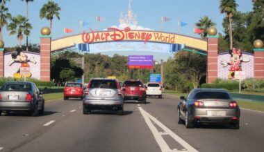 Guests arrive in cars beneath the vibrant Walt Disney World entrance, flanked by palm trees and beloved Disney World characters. Disney World weather forecast