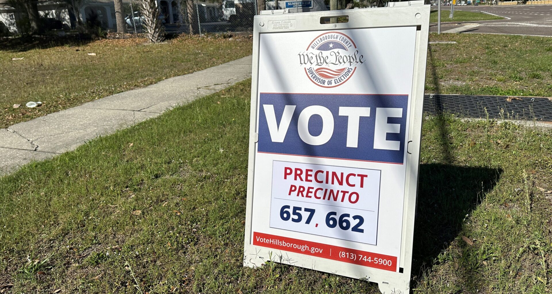 A white barrier stands in a grassy field that says "We The People" and "Vote." Election
