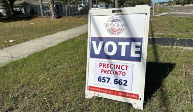 A white barrier stands in a grassy field that says "We The People" and "Vote." Election