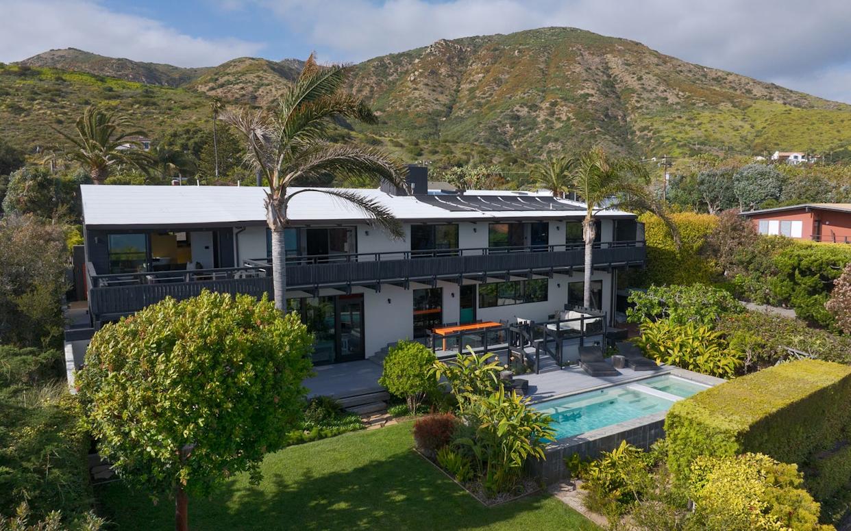 Modern house with a pool surrounded by lush greenery and mountains in the background.