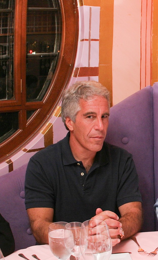 Jeffrey Epstein in a black polo shirt, seated at a table.