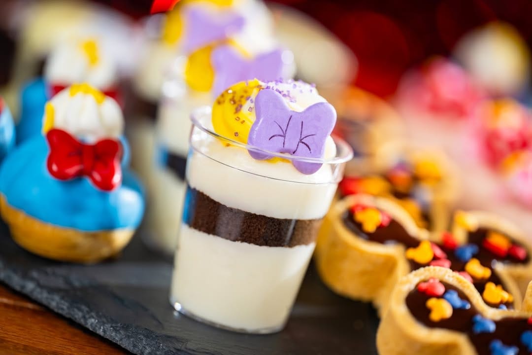 The Daisy mousse appears to come with a layered cookies and cream mousse with a dollop of white and yellow frosting on top, with a purple candy bow.