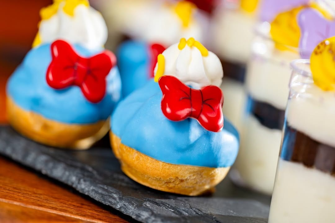 The Donald cream puff is coated in a layer of purple icing. On top of the puff is a dollop of white frosting with yellow detailing, and a red candy bowtie sits at the front. It looks a bit like a bath-time rubber ducky.