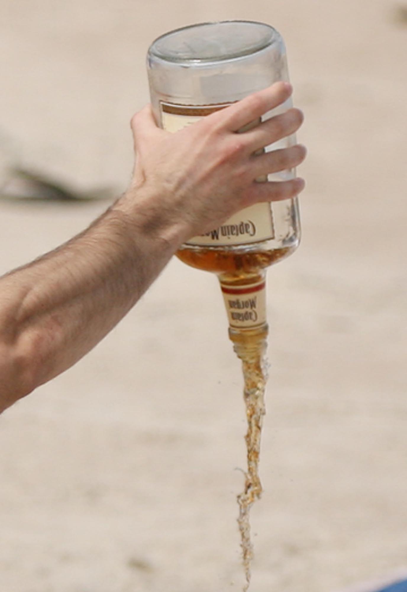 A spring breaker pours his booze onto the sand under...