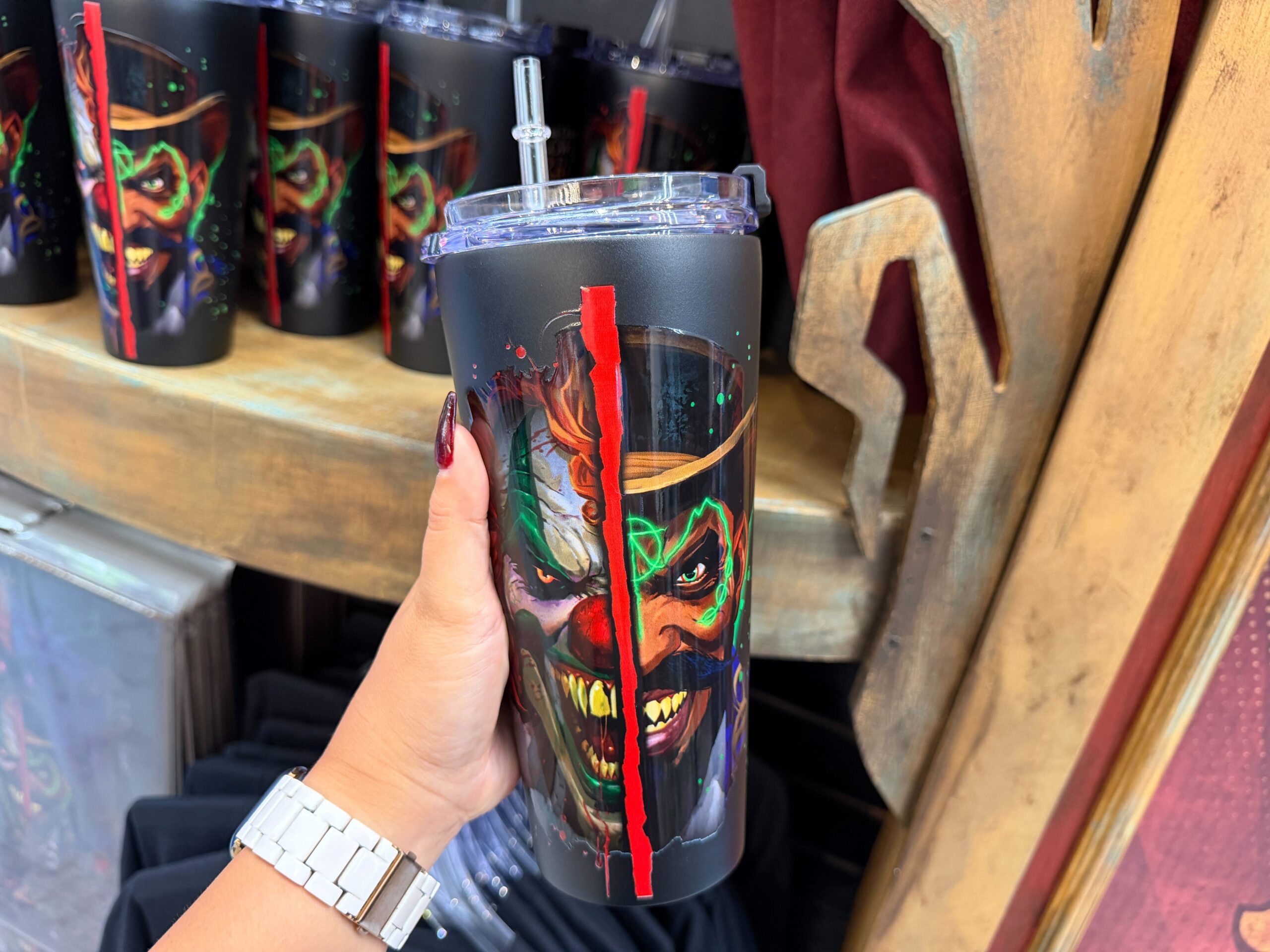 Jack The Clown and Dr. Oddfellow's split faces are on the front of this black tumbler. The back of the tumbler says "Universal Orlando Halloween Horror Nights 2026." It comes with a clear, acrylic straw.