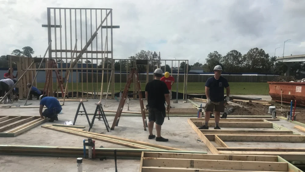 Volunteers work on laying a home's foundation and putting up walls.