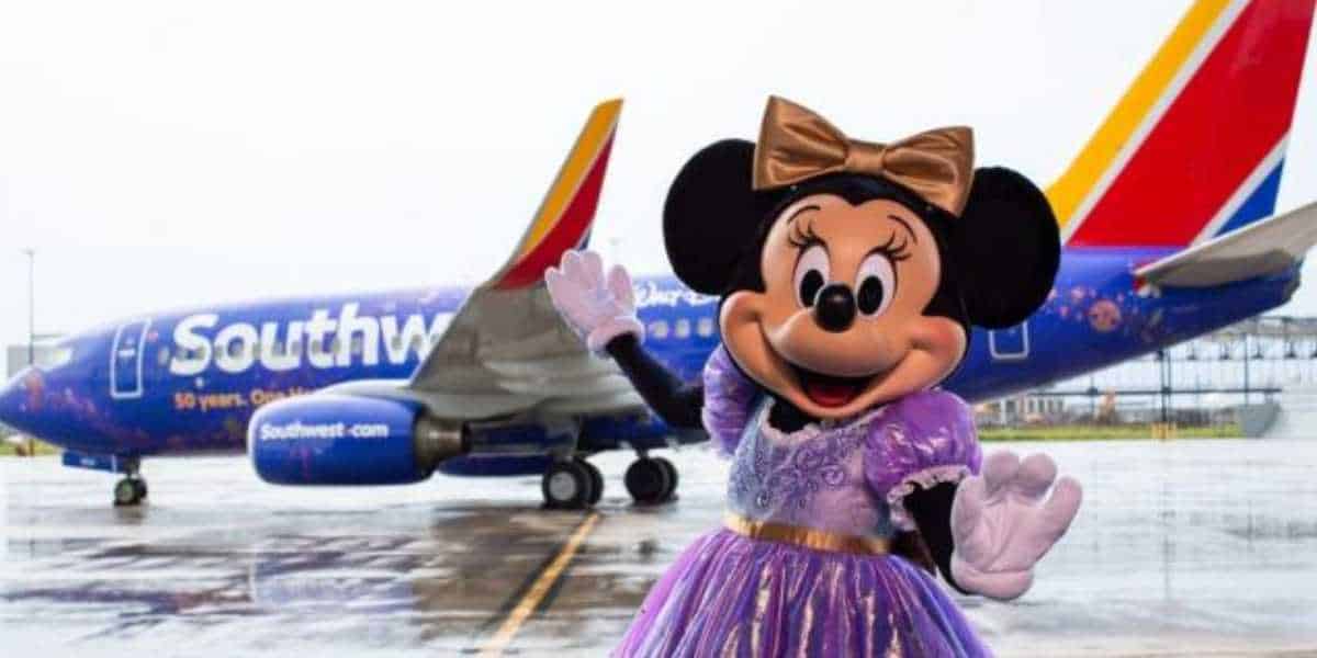 Minnie Mouse in a purple dress waves on the wet tarmac as a Southwest plane arrives, greeting Disney World guests with magic.