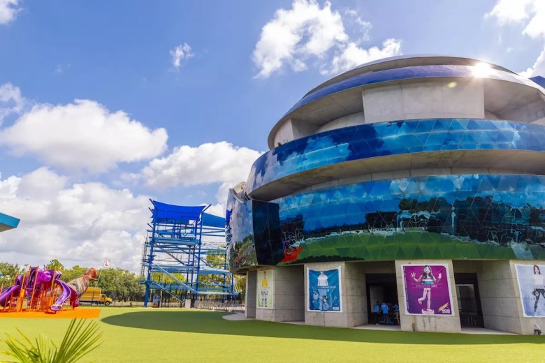 Exterior view of the Museum of Science and Industry (MOSI) in Tampa, Florida, showing the blue dome building, ropes course, and dinosaur playground.