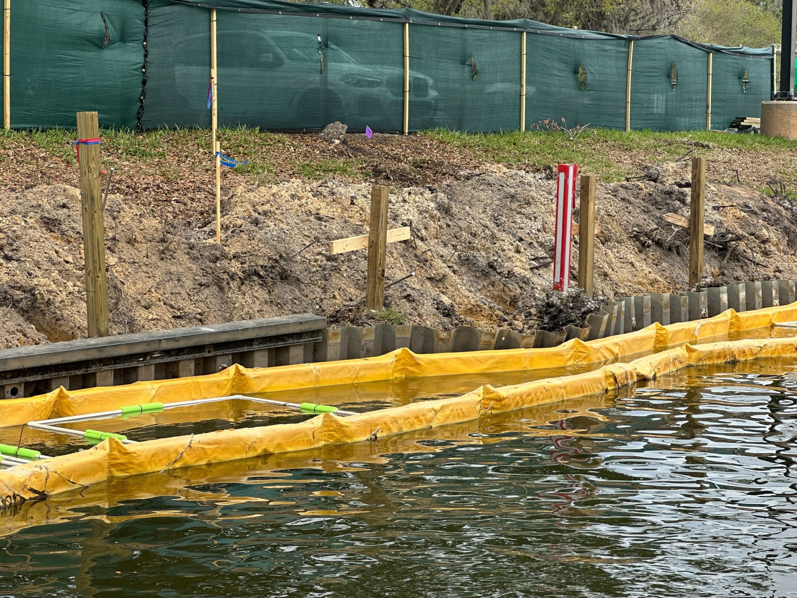 These yellow boundary markers appear to be spacing out new sections of wall to be inserted along the riverbank. Stakes are in place behind the existing barriers. We can see that the top portion of the barriers has been removed from some of them, causing them to bow out or in as seen above.