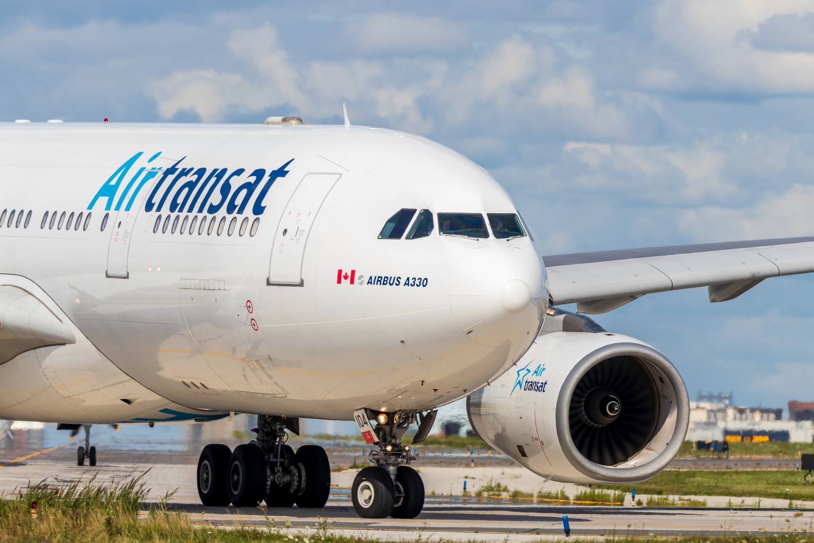 Front view of an Air Transat plane at an airport with a cloudy sky in the background