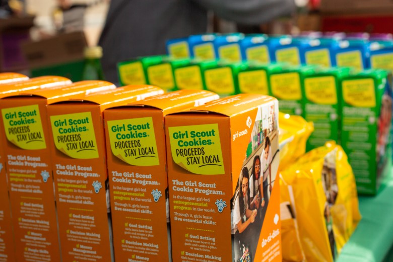 Rows of colorful Girl Scout Cookie boxes lined up for sale, with orange do-si-dos boxes in the foreground.