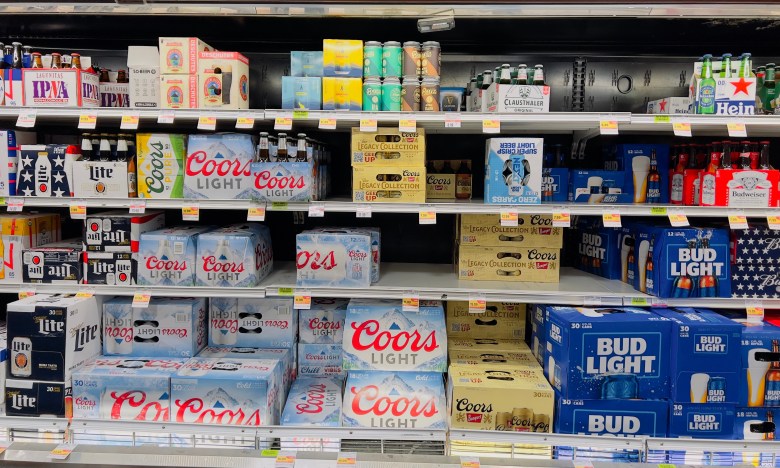 Shelves of American-made beer in a grocery store cooler, including packs of Coors Light and Bud Light, highlighting Florida's new beer tax breaks.