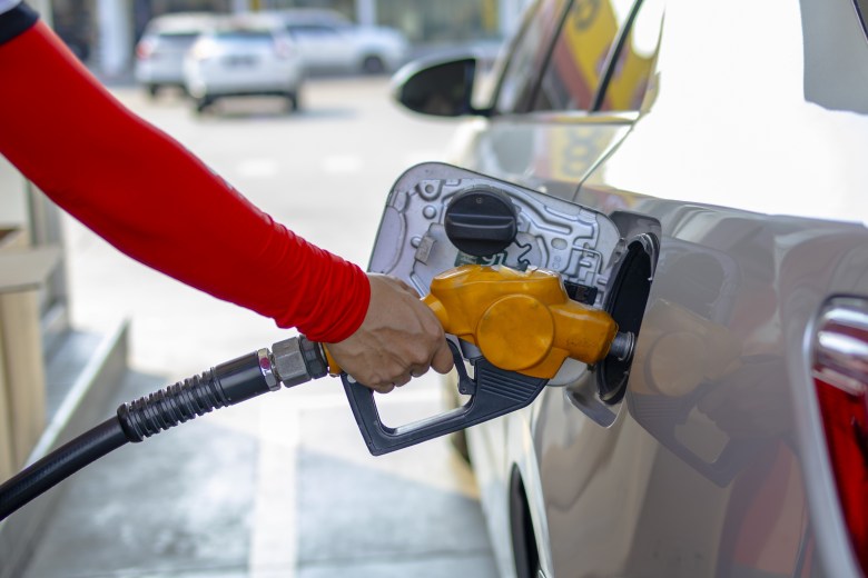Close-up of a person's hand holding a yellow fuel nozzle while refueling a car at a gas station