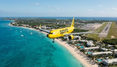 Spirit Airlines jet approaching Grand Cayman over turquoise water and Seven Mile Beach.