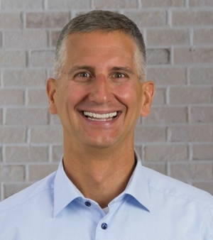 Man set in front of a white brick wall smiling at camera.