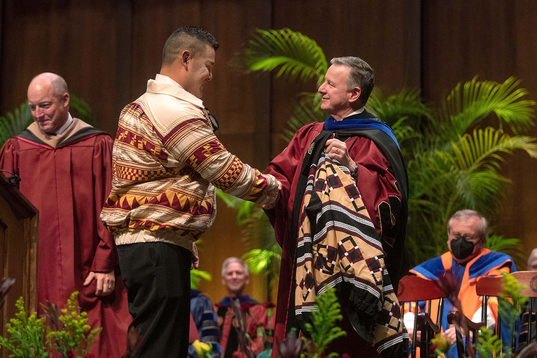 Two people shake hands, one of them wearing regalia