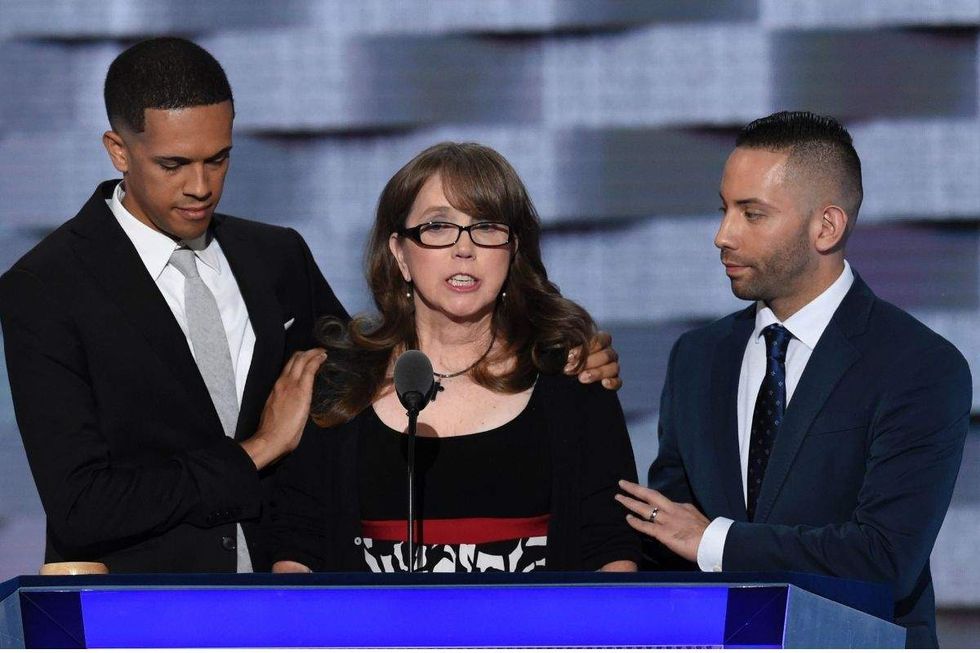 three people, two men and one woman ,standing behind a large blue lectern onstage at a convention