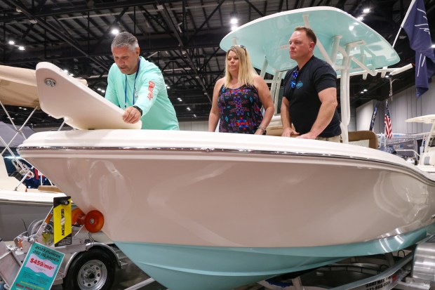 Mark Thomason shows Michelle Koreger and Aaron Murphy the features on a 2025 Pioneer Islander boat on display by Boat Max Worldwide. (Rich Pope/Orlando Sentinel)