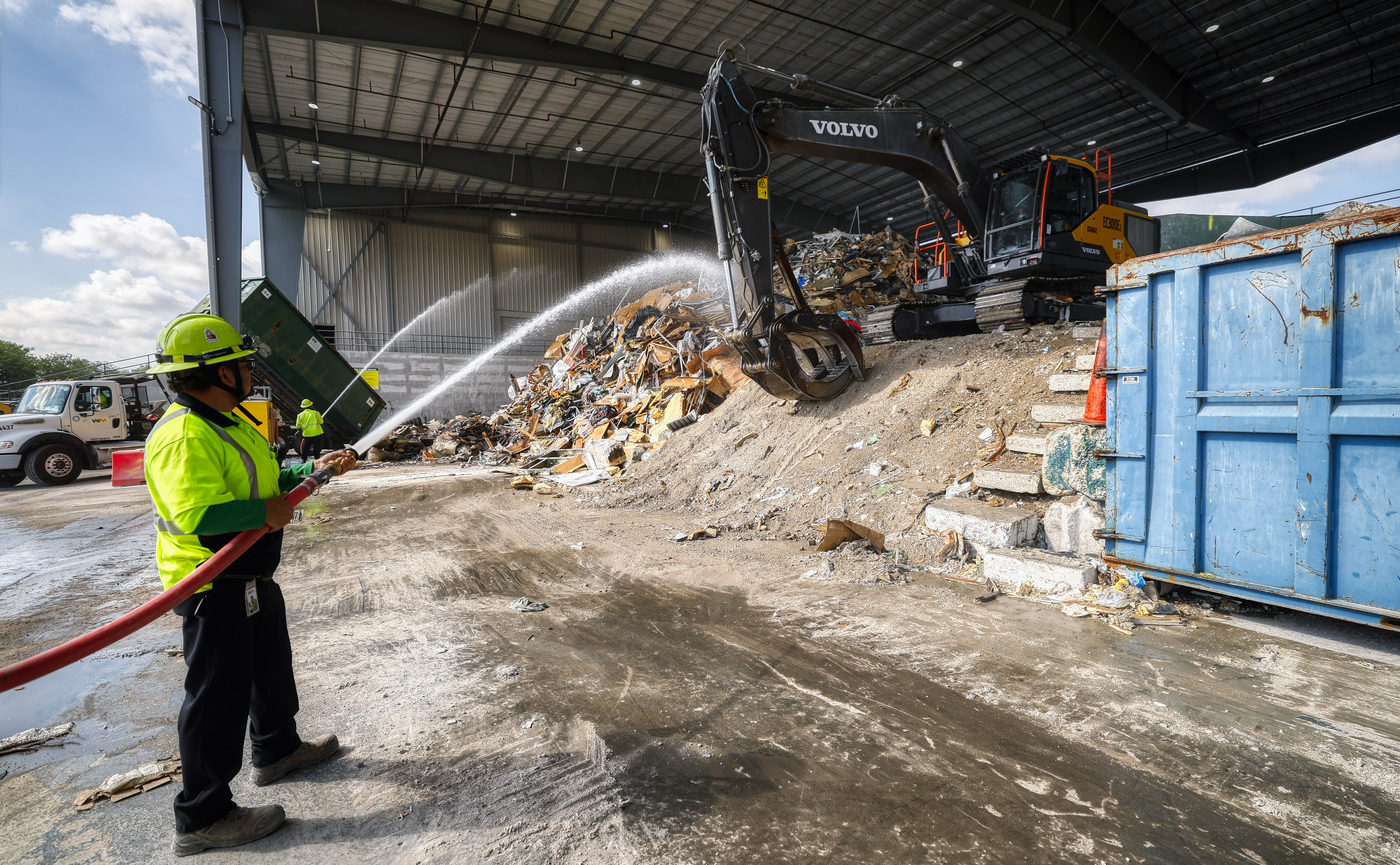 Workers hose down the pile of construction debris during a...