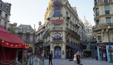 Guests stroll and snap photos in a city square with ornate fa&ccedil;ades, a Quidditch sign, and Daily Recap display&mdash;no castle in sight.