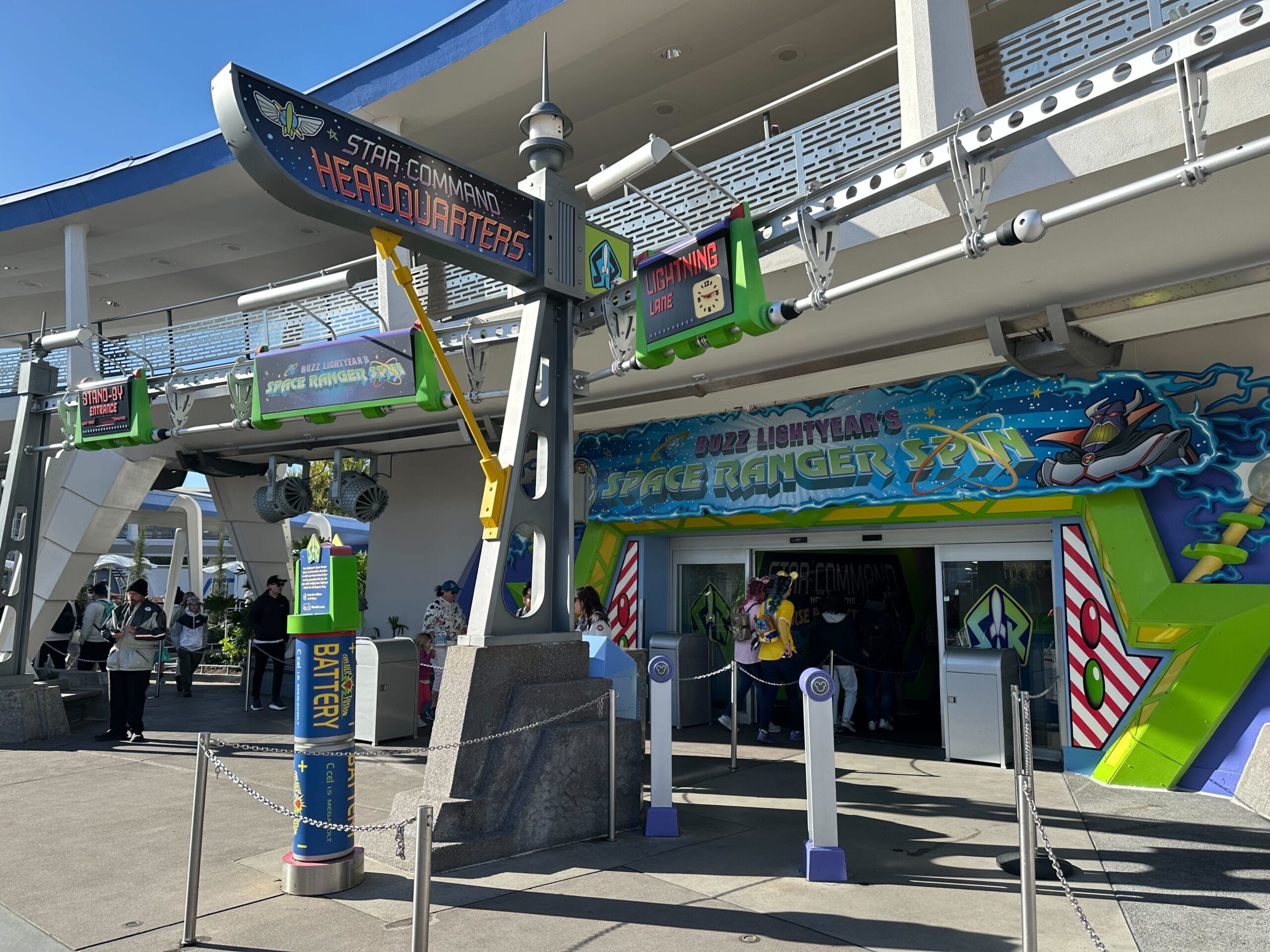 Entrance to Buzz Lightyear's Space Ranger Spin at a theme park, featuring colorful signage with a space motif and people waiting in line.