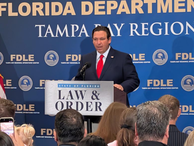 Florida Governor Ron DeSantis speaking at a podium during a press conference at the Tampa Bay Regional Operations Center.