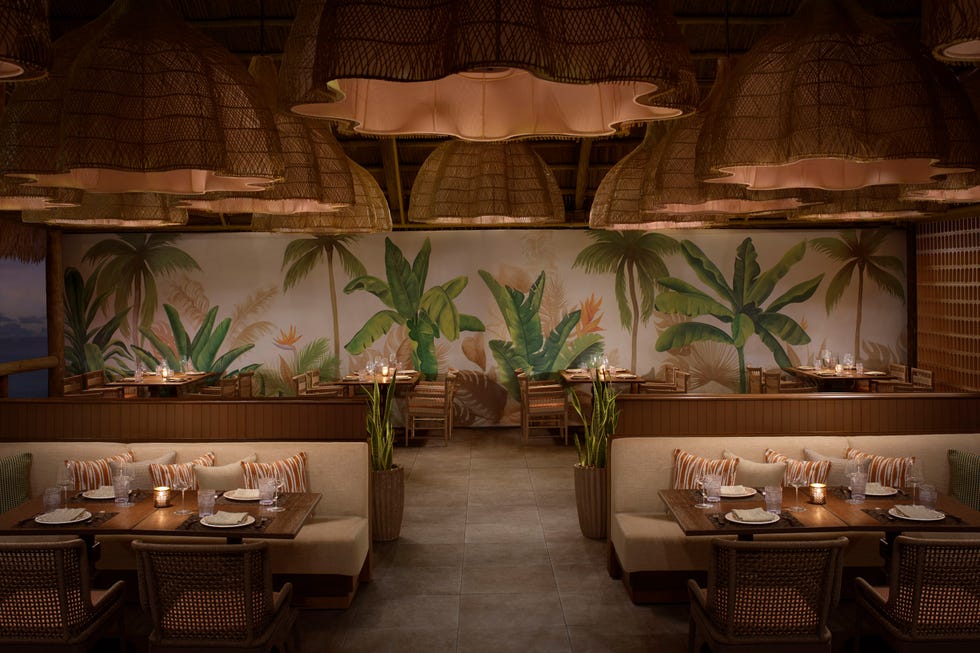 Interior of a tropical-themed restaurant featuring woven light fixtures and plant murals.