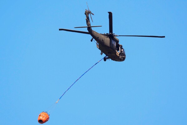 A helicopter carries water to the Brantley Highway 82 fire, Thursday, April 23, 2026, near Nahunta, Ga. (AP Photo/Mike Stewart)
