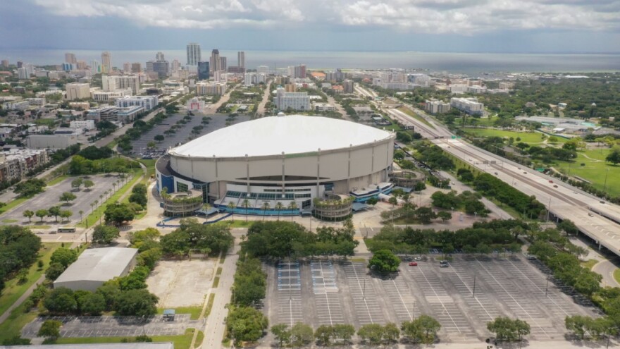 An aerial view of a domed baseball stadium with a wide shot of a highway to the right and buildings to the left