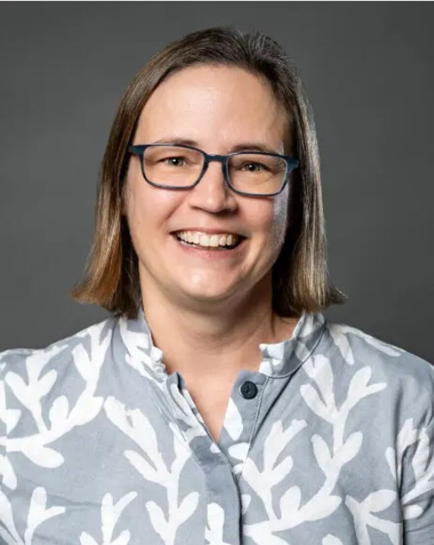 Woman with short brown hair, glasses and gray blouse smiling into the camera