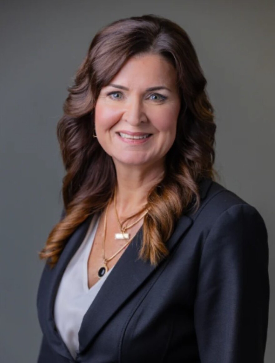 Woman with long brown hair and blue blazer smiling into the camera