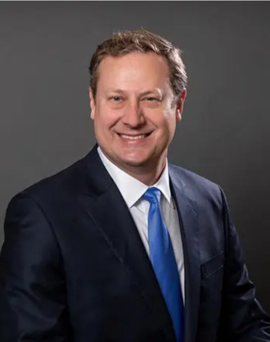Man with brown hair and blue suit and tie smiling into the camera