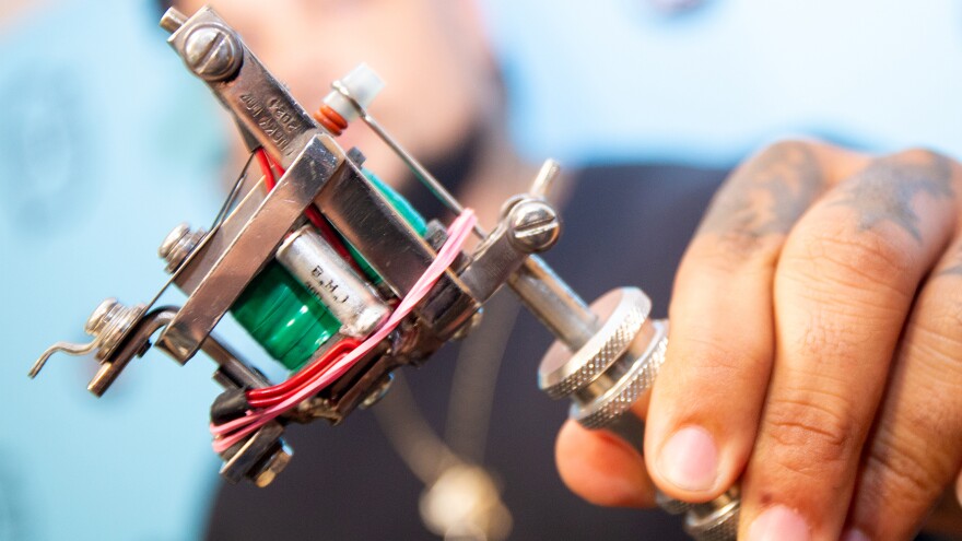 A close up of a stainless steel tattoo machine with green coils. 