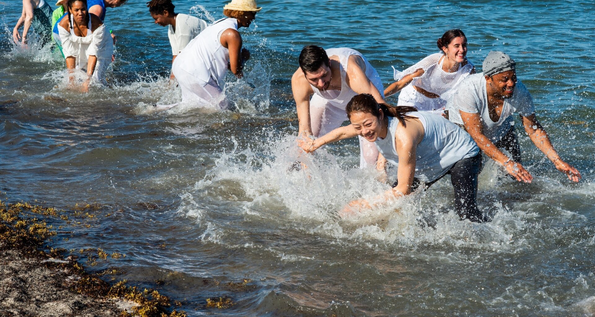 photo of dancers wearing white and scooping ocean water as part of a choreographed dance