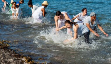 photo of dancers wearing white and scooping ocean water as part of a choreographed dance