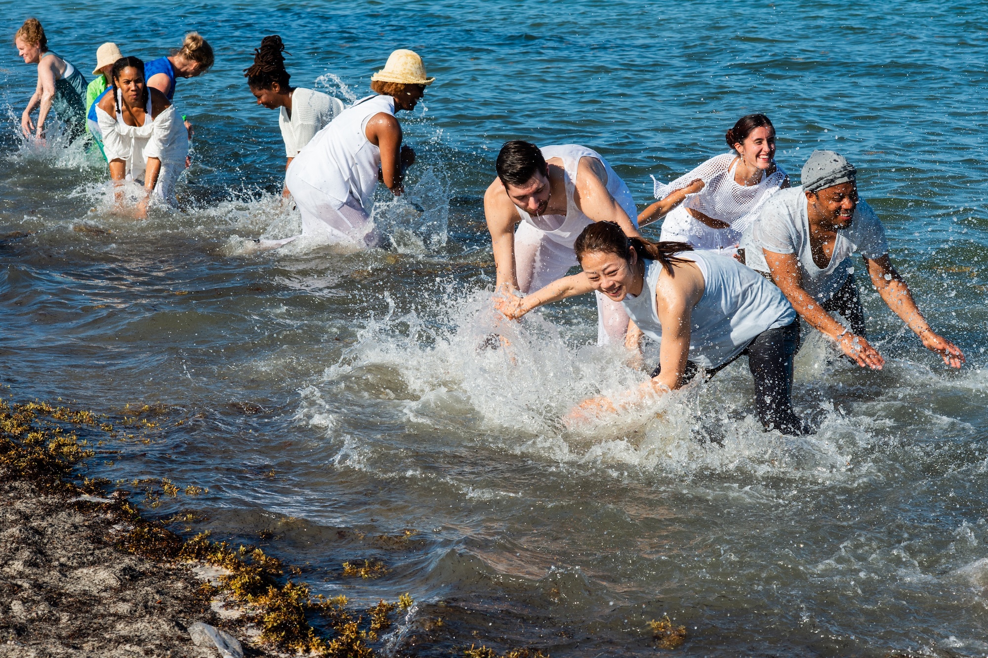photo of dancers wearing white and scooping ocean water as part of a choreographed dance