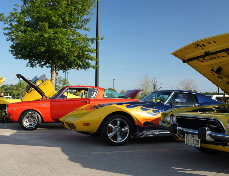 Custom classic cars including a flame-painted Corvette and a yellow Dodge Challenger on display at the Hot Wheels Legends Tour.